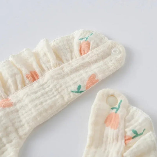 Détail d’un bavoir bébé en coton doux avec motifs fleurs orange et fermeture bouton pression, tissu respirant et confortable pour nourrisson