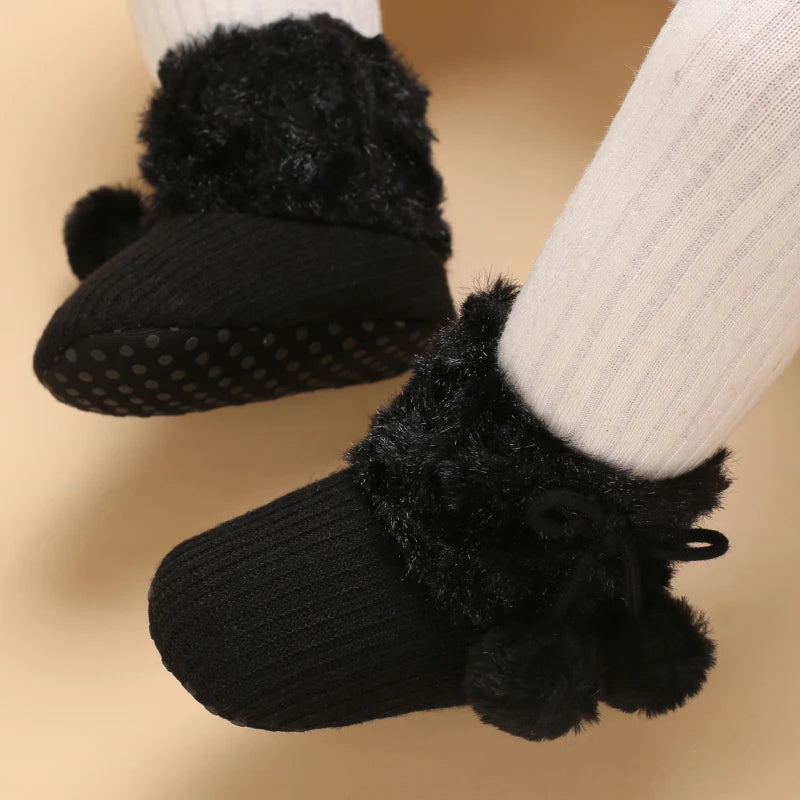 Bottines bébé noires portées, fourrure noire et pompons assortis, modèle chaud d’hiver.