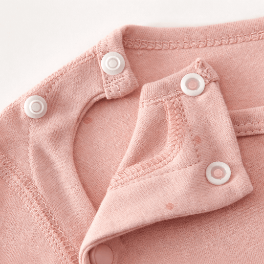 Gros plan sur l’encolure d’un pyjama pour bébé rose avec boutons pression blancs et coutures apparentes, montrant le système d’ouverture sur le devant.