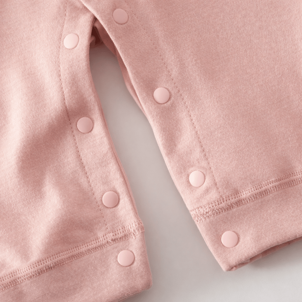 Gros plan sur le bas d’un pyjama pour bébé rose avec boutons pression le long des jambes et coutures apparentes, montrant le système d’ouverture pour le change.