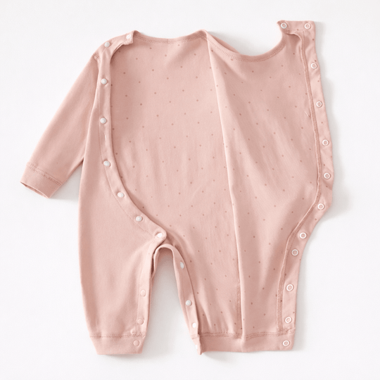 Pyjama pour bébé rose clair à manches longues avec petits pois discrets et ouverture complète à boutons pression sur le devant, présenté à plat sur un fond clair.