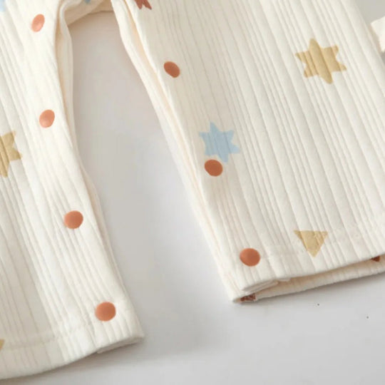 Zoom sur tissu barboteuse bébé en coton doux texturé avec motifs étoiles et formes géométriques, vêtement nourrisson confortable.