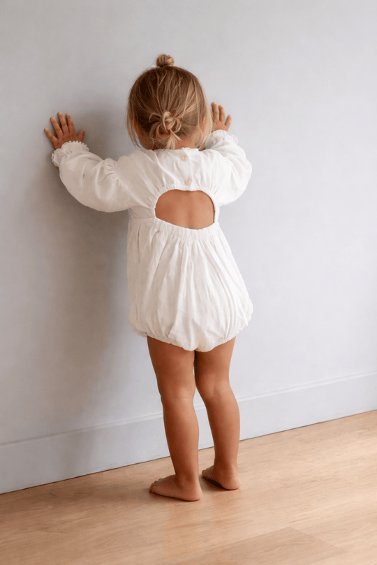 Petite fille en barboteuse blanche manches longues avec ouverture dans le dos, combinaison bébé en coton style bohème chic, vue de dos.