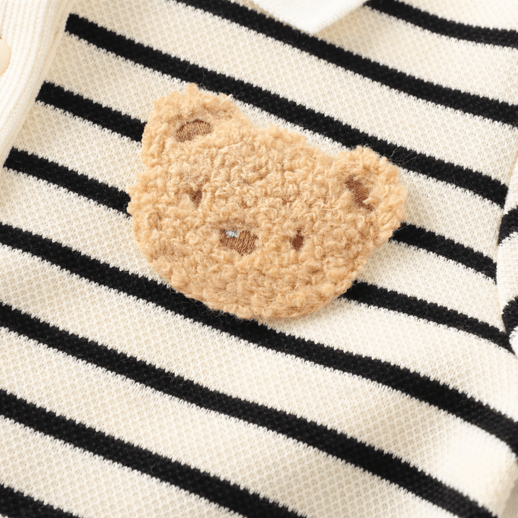 Gros plan sur un patch ourson brodé en tissu pelucheux cousu sur une barboteuse bébé rayée noir et beige en coton doux.