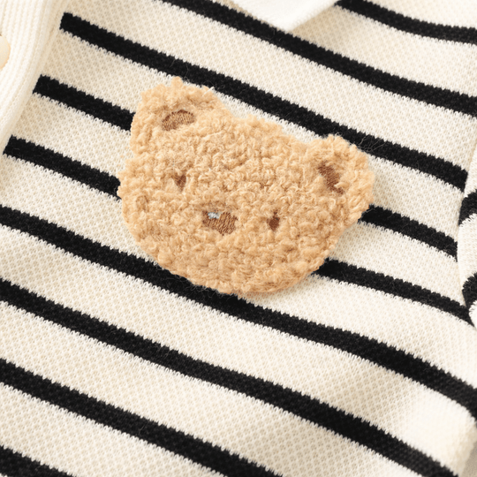 Gros plan sur un patch ourson brodé en tissu pelucheux cousu sur une barboteuse bébé rayée noir et beige en coton doux.