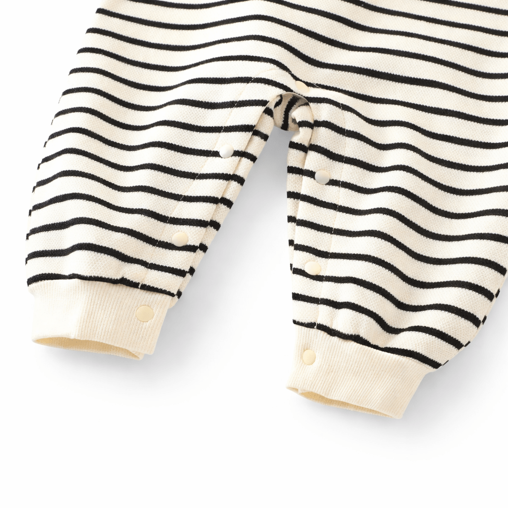 Détail du bas d’une barboteuse bébé rayée noir et blanc en coton avec boutons pression pour le change, vêtement confortable pour enfant sur fond blanc