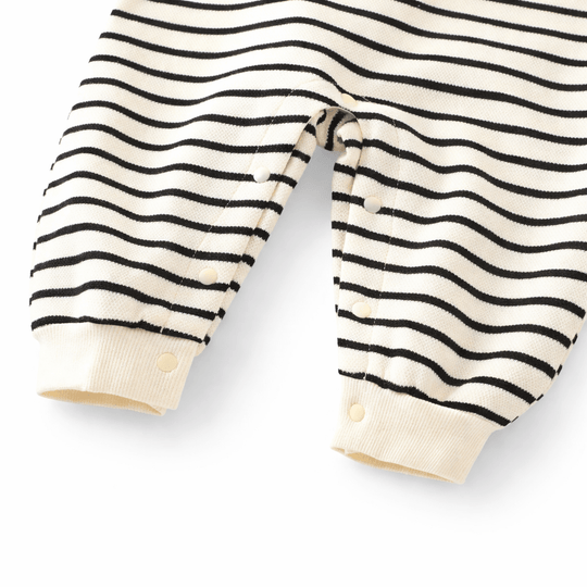 Détail du bas d’une barboteuse bébé rayée noir et blanc en coton avec boutons pression pour le change, vêtement confortable pour enfant sur fond blanc