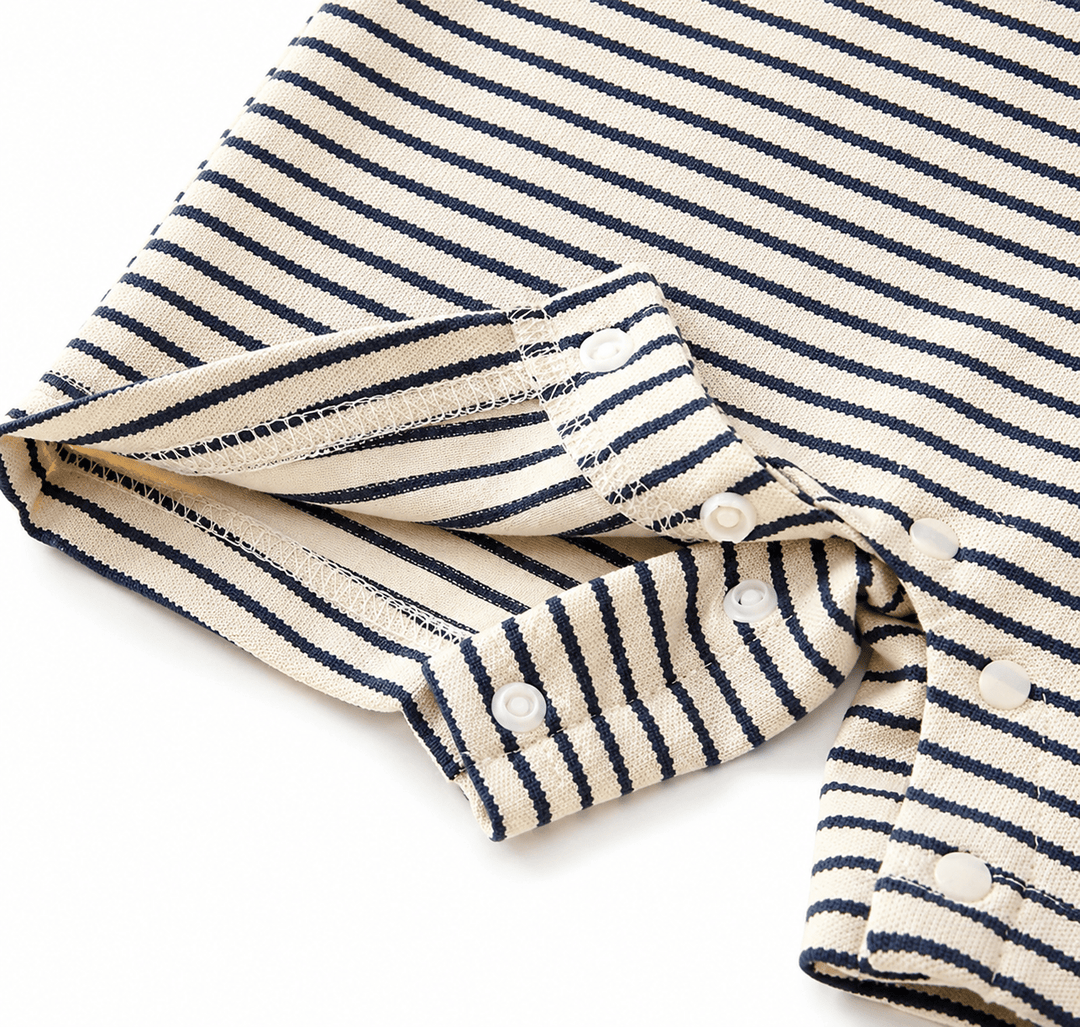 Gros plan sur les boutons-pression et les finitions d’une barboteuse bébé à rayures bleu marine et écru, mettant en valeur la qualité des coutures et du tissu doux