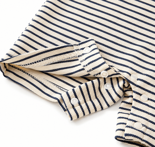 Gros plan sur les boutons-pression et les finitions d’une barboteuse bébé à rayures bleu marine et écru, mettant en valeur la qualité des coutures et du tissu doux