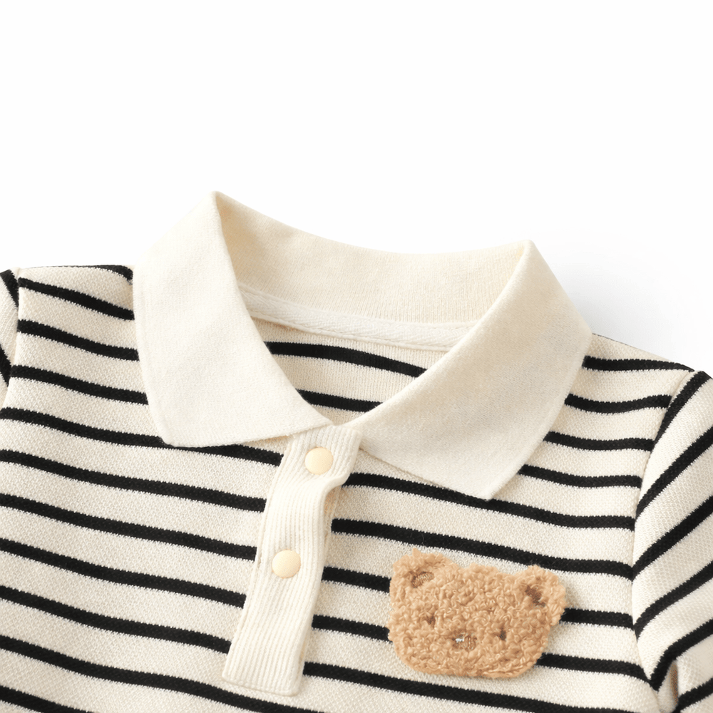 Détail du col d’une barboteuse bébé rayée noir et blanc en coton avec boutons pression et motif ourson, vêtement confortable pour enfant sur fond blanc.