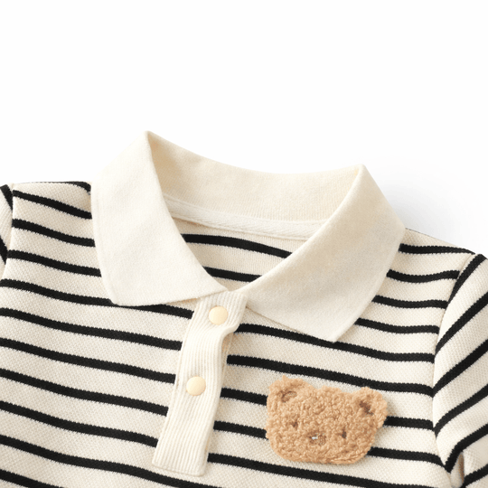 Détail du col d’une barboteuse bébé rayée noir et blanc en coton avec boutons pression et motif ourson, vêtement confortable pour enfant sur fond blanc.