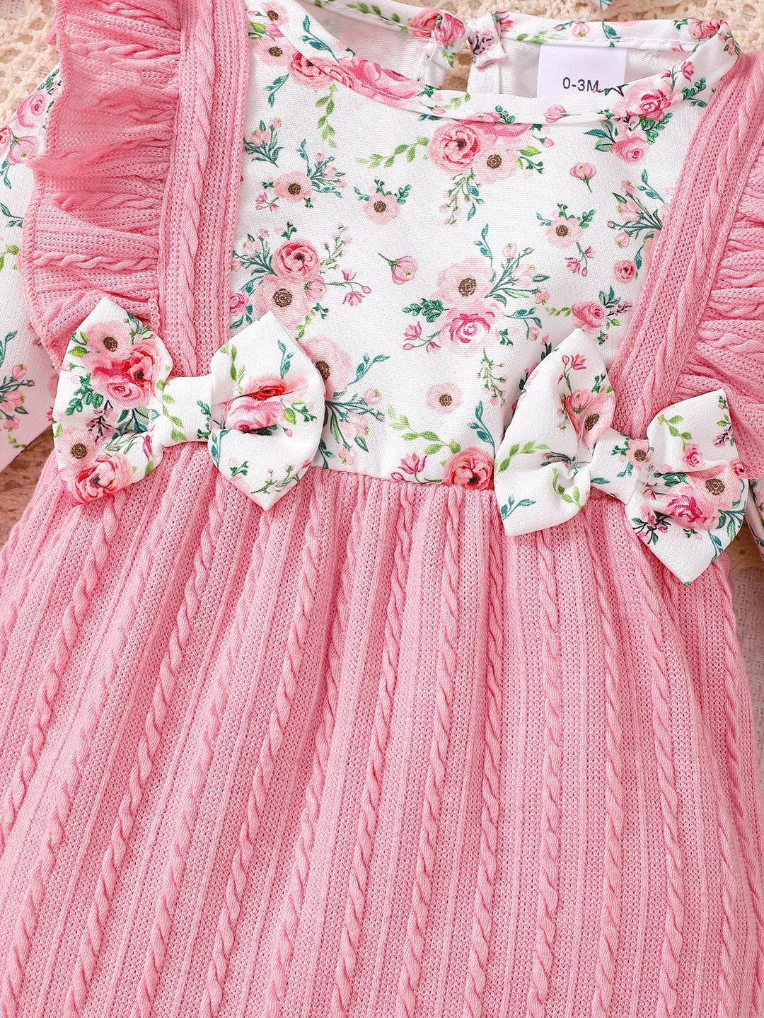 Gros plan sur la barboteuse bebe rose KaliNatur avec haut fleuri et noeuds decoratifs, tissu doux a motifs floraux et volants elegants.
