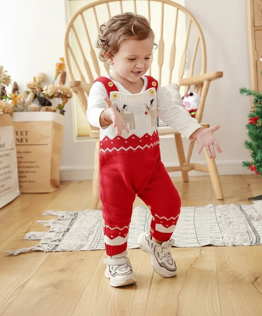 Bebe souriant portant une barboteuse de Noel rouge et blanche en tricot avec motifs rennes, manches longues, boutons dores et motif festif, photographie lifestyle KaliNatur.
