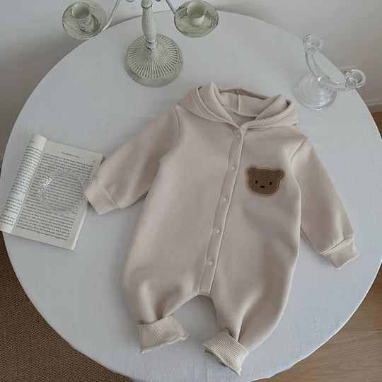 Combinaison bébé beige à capuche avec ourson, présentée sur une table blanche.