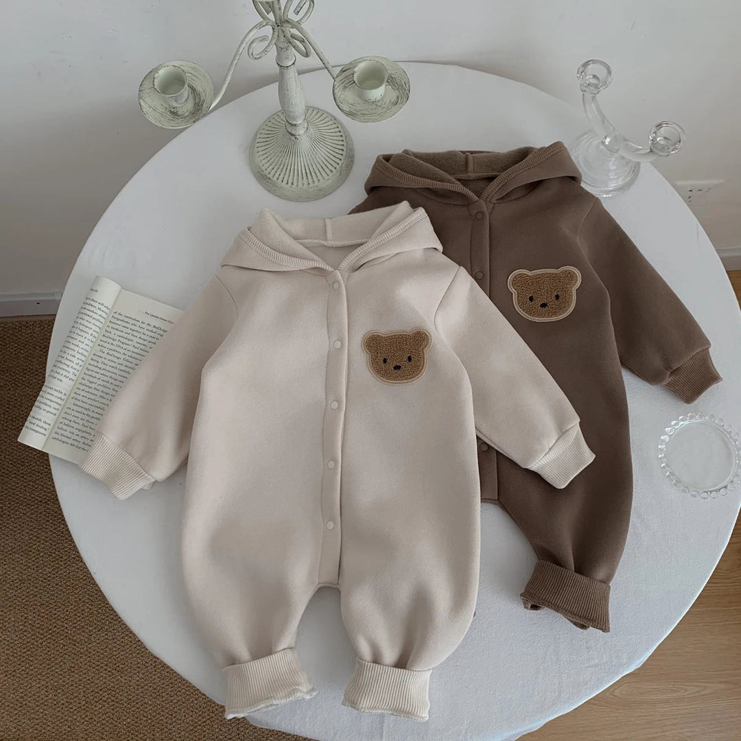 Duo de combinaisons bébé beige et marron avec capuche et patch ourson, présentées côte à côte.
