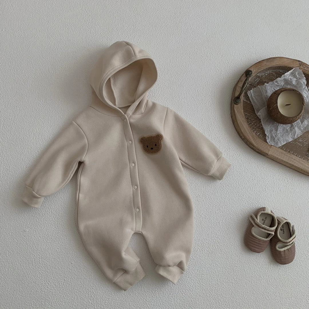 Combinaison bébé beige à capuche avec patch ourson, présentée avec des chaussons assortis.