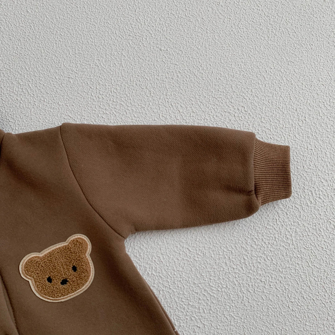 Détail de la manche et du patch ourson sur une combinaison bébé marron.