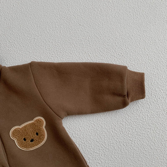 Détail de la manche et du patch ourson sur une combinaison bébé marron.