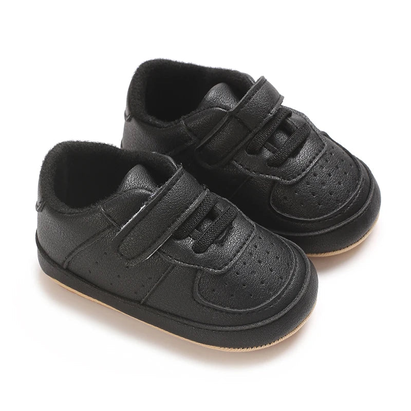 Chaussures premiers pas bébé noires à fermeture scratch, légères et stables, adaptées aux premiers pas et à un usage quotidien.

