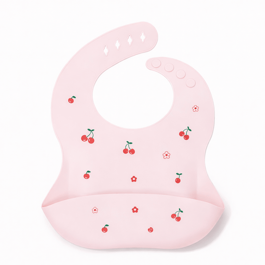 Bavoir bébé en silicone rose avec poche récupératrice, décoré de petites cerises rouges et fleurs, sur fond blanc