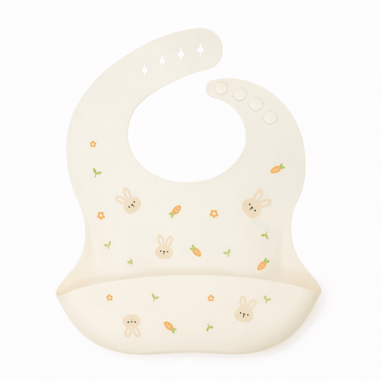 Bavoir bébé en silicone beige avec poche récupératrice, décoré de petits lapins, carottes et fleurs, sur fond blanc
