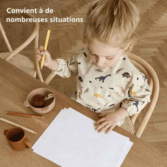 Bébé portant un bavoir imperméable à manches longues motif dinosaures en train de dessiner à table, protection anti-taches