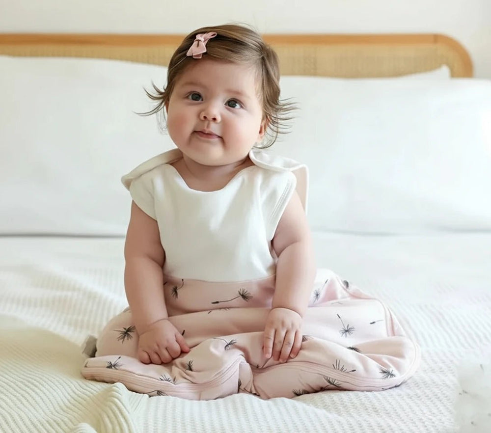 Bébé assis sur un lit portant une gigoteuse beige à motifs pissenlits en coton, collection Kalinatur
