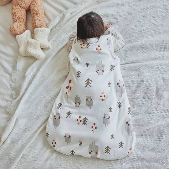 Bébé allongé sur le ventre portant une gigoteuse blanche en coton à motifs de forêt et d’animaux, collection Kalinatur.
