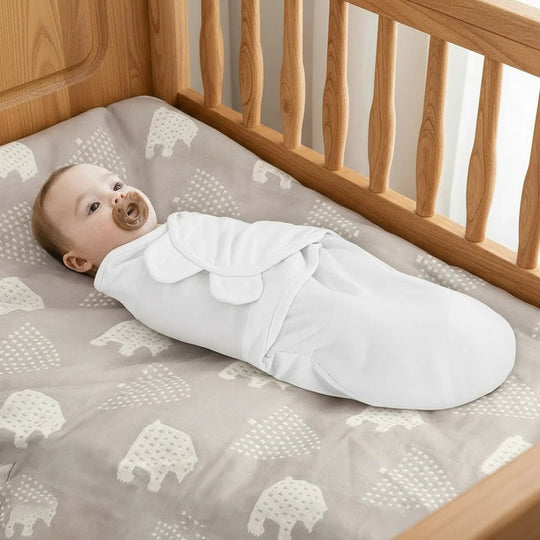 Bébé allongé dans un berceau portant une gigoteuse d’emmaillotage blanche en coton, douce et sécurisée – Kalinatur.