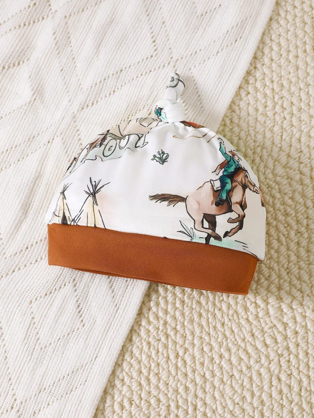 Bonnet bébé Western Kalinatur assorti à la combinaison, imprimé chevaux et bottes, tissu doux et confortable avec bord marron.
