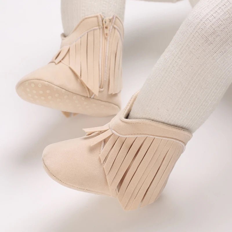 Bottines bébé style bohème en suédine beige, décorées de franges et équipées d’une fermeture zippée + scratch. Semelle antidérapante, confort et style à la fois.