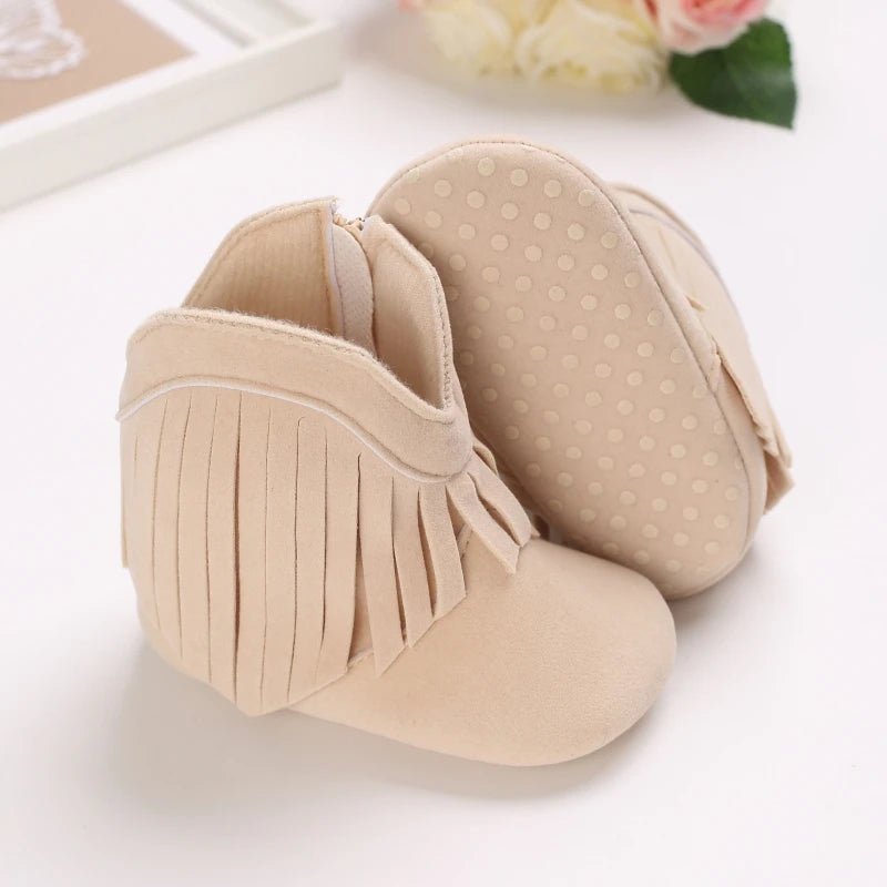 Bottines bébé en suédine beige, ornées de jolies franges et dotées d’une semelle souple antidérapante. Un style bohème chic pour garder bébé confortable et sécurisé.