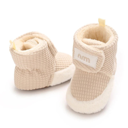 Paire de bottines bébé en tissu gaufré, douces et chaudes, avec fermeture sécurisée et base fourrée. Idéales pour garder les petits pieds bien protégés en hiver.