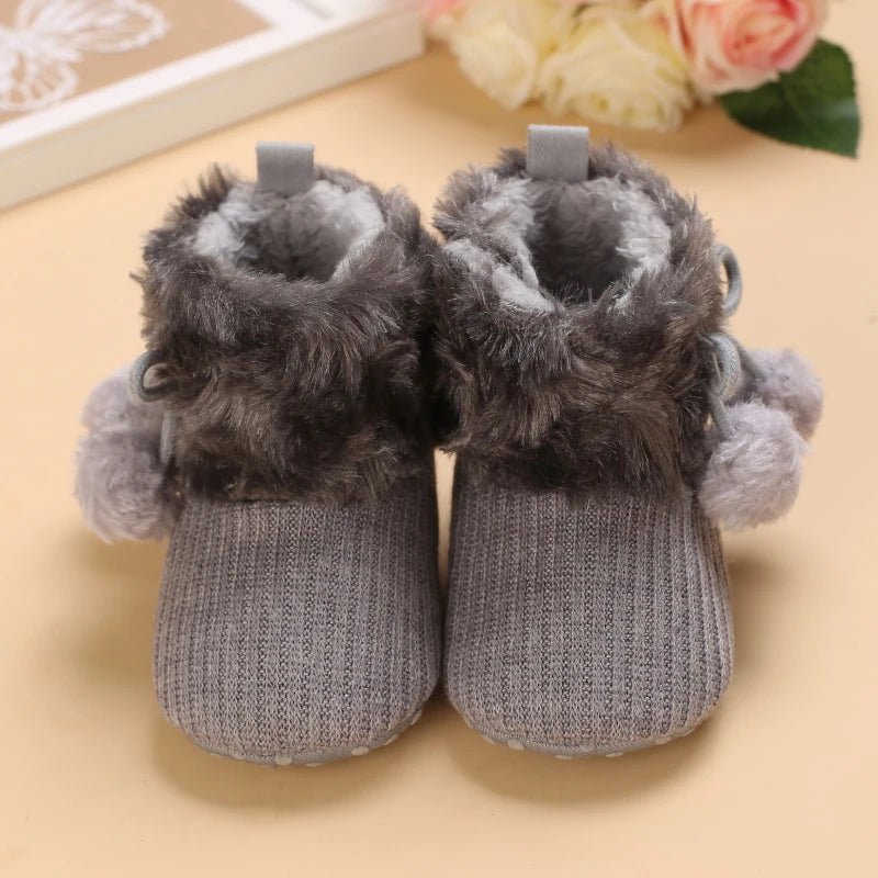 Bottines bébé gris pompon vues de face, fourrure moelleuse et pompons décoratifs.