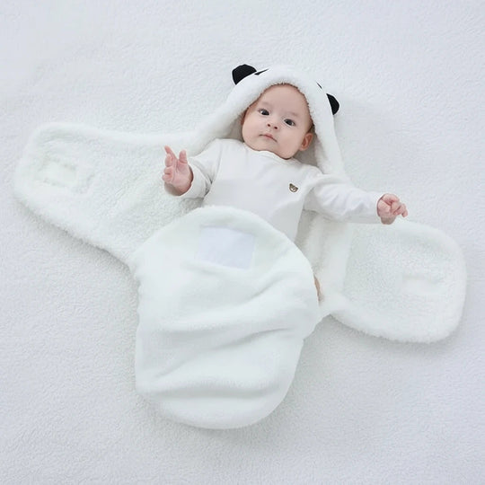 Bébé allongé sur un plaid blanc, emmailloté dans une couverture panda blanche Kalinatur ouverte, douce et chaude, avec capuche à oreilles noires.