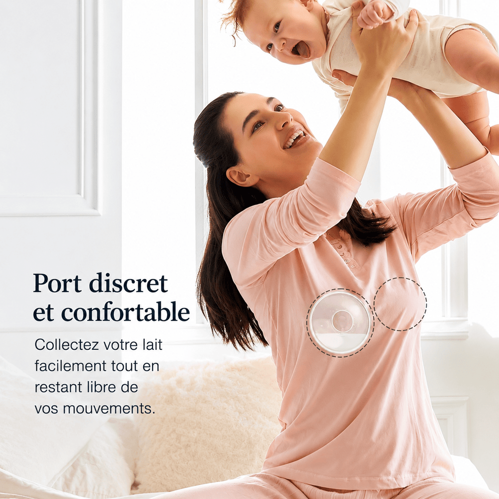 Jeune maman souriante jouant avec son bébé dans une chambre lumineuse tout en portant discrètement un collecteur de lait maternel sous ses vêtements. Illustration du confort, de la discrétion et de la liberté de mouvement pendant l’allaitement