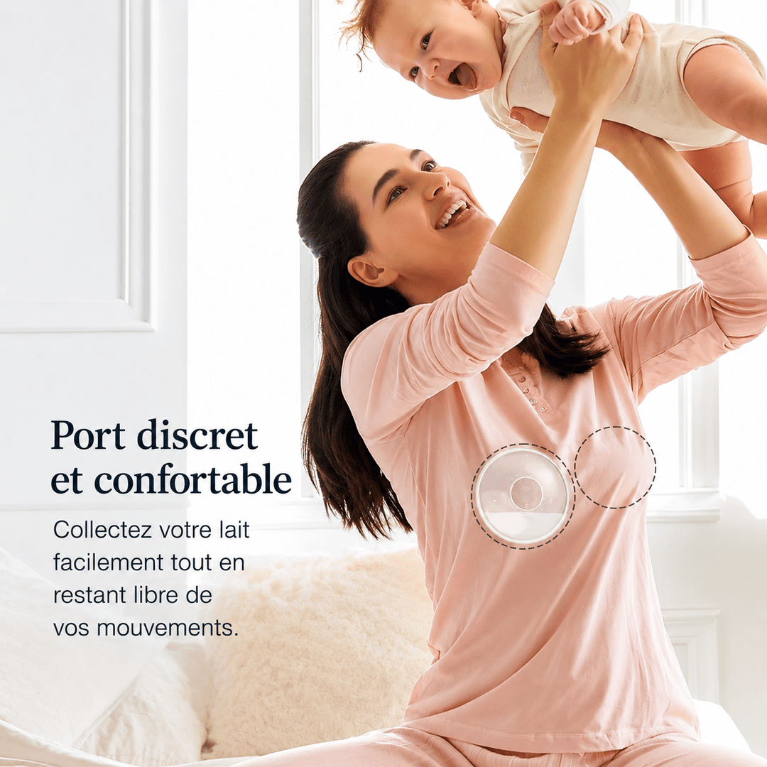 Jeune maman souriante jouant avec son bébé dans une chambre lumineuse tout en portant discrètement un collecteur de lait maternel sous ses vêtements. Illustration du confort, de la discrétion et de la liberté de mouvement pendant l’allaitement