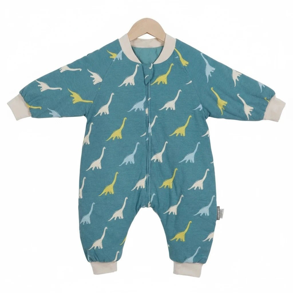 Gigoteuse à jambes Kalinatur pour bébé en coton bio, couleur bleu canard, imprimée de petits dinosaures jaunes et blancs, suspendue sur un cintre en bois.
