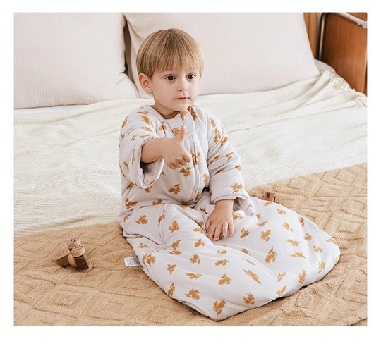 Petit garçon assis sur un lit beige portant la gigoteuse d’hiver Kalinatur à motifs de feuilles dorées, confortable et chaude pour la saison froide.