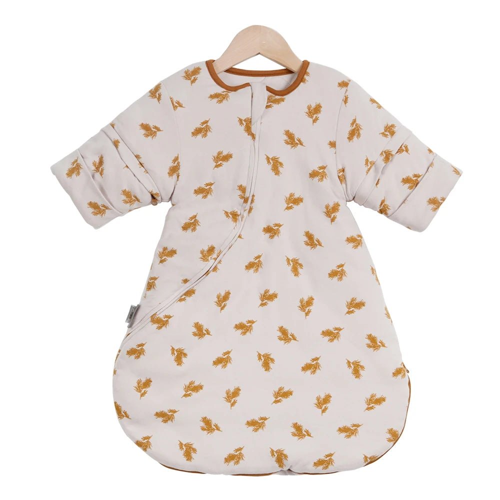 Gigoteuse bébé d’hiver à manches longues, couleur beige à motifs de feuilles moutarde, suspendue sur cintre en bois, marque Kalinatur, douce et chaude pour un sommeil confortable.
