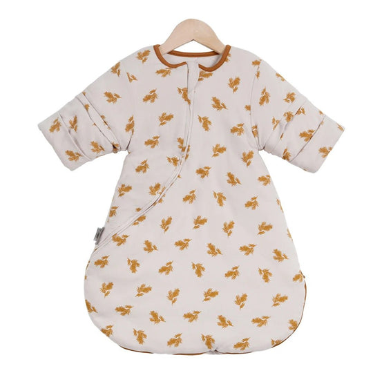 Gigoteuse bébé d’hiver à manches longues, couleur beige à motifs de feuilles moutarde, suspendue sur cintre en bois, marque Kalinatur, douce et chaude pour un sommeil confortable.

