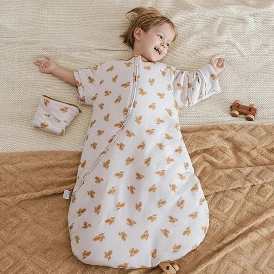 Enfant allongé sur un lit portant la gigoteuse d’hiver Kalinatur à manches longues et motifs de feuilles dorées, douce et confortable pour des nuits bien au chaud.