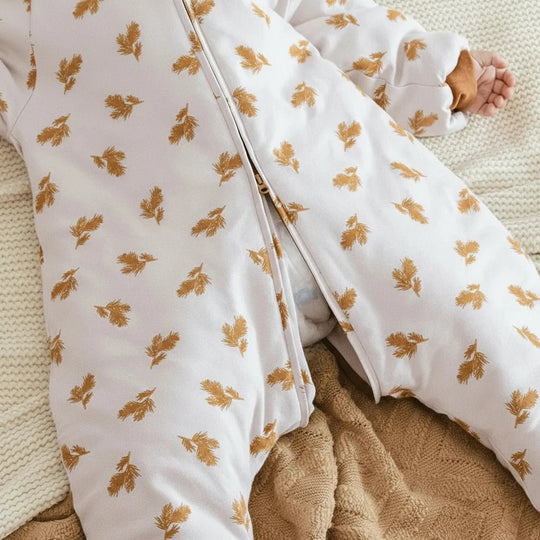 Détail de la gigoteuse à jambes Kalinatur avec fermeture éclair centrale, motif feuilles dorées sur fond beige, tissu doux et chaud pour bébé.