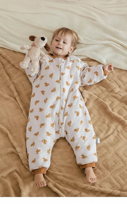 Enfant jouant sur un lit beige, vêtu d’une gigoteuse à jambes Kalinatur motif feuilles automnales, chaude et confortable pour l’hiver.