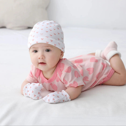 Bébé fille en body rose à cœurs Kalinatur, bonnet et moufles assortis, en position sur le ventre.