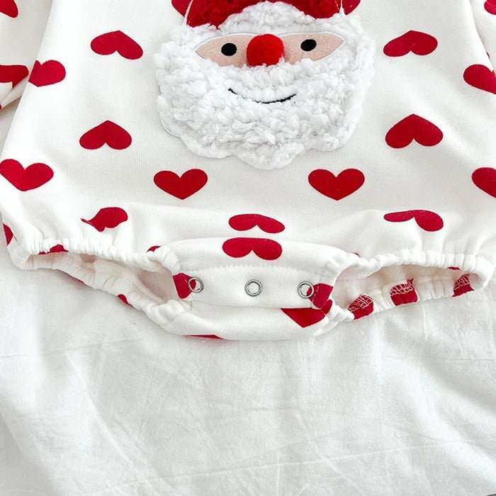 Détail du body bébé blanc Kalinatur avec imprimé de cœurs rouges, motif Père Noël en relief et boutons-pression à l’entrejambe.