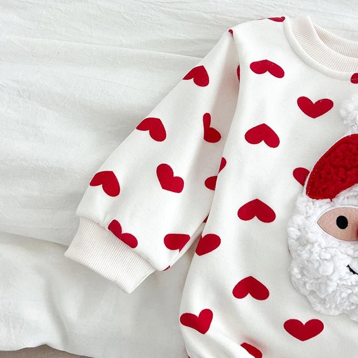 Gros plan sur la manche du body bébé blanc Kalinatur décoré de cœurs rouges, avec détail du motif Père Noël en relief.