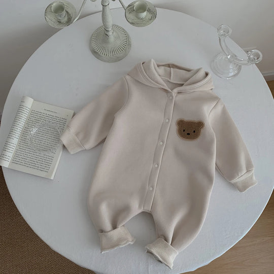 Combinaison bébé beige à capuche avec ourson, présentée sur une table blanche.