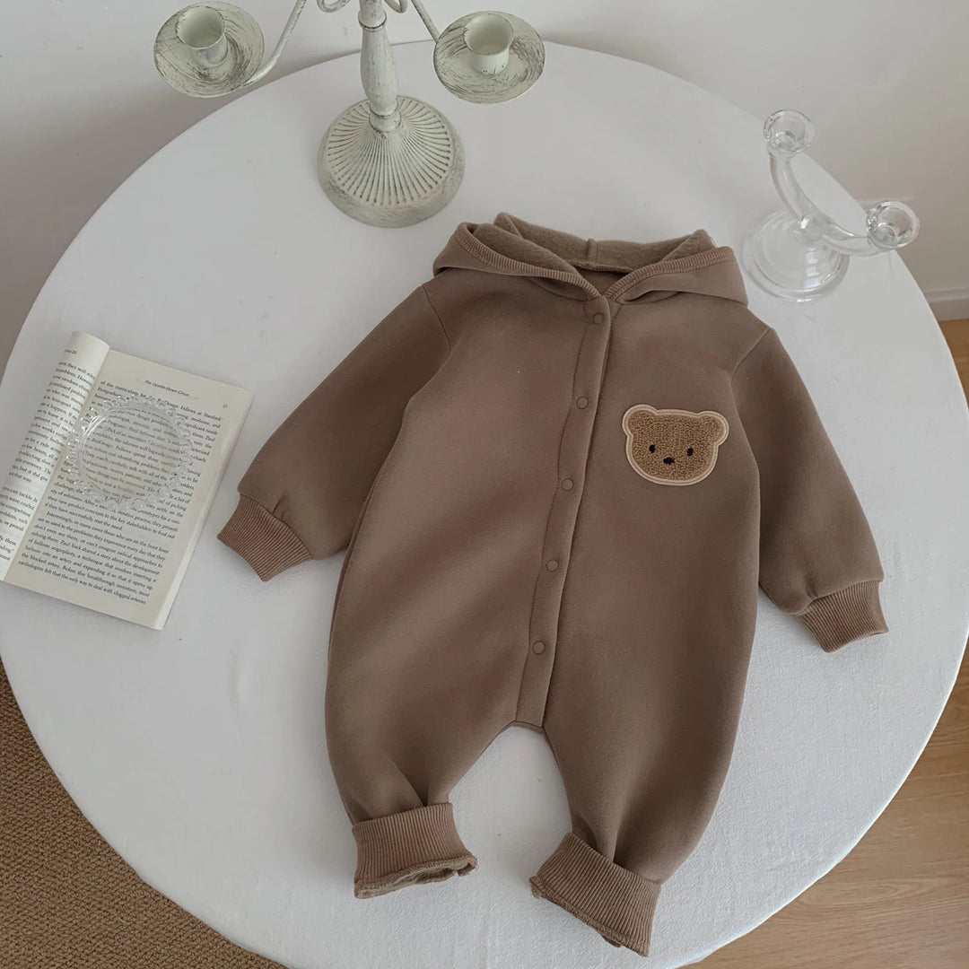 Combinaison bébé marron avec capuche et ourson, posée sur une table décorative.