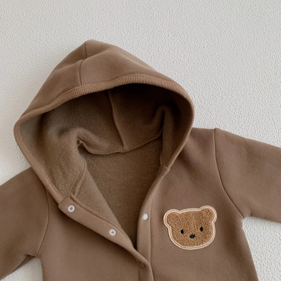 Zoom sur la capuche et le patch ourson d’une combinaison bébé marron.